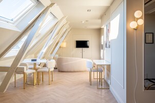 Um quarto moderno no estilo loft, com teto alto, claraboias, TV de tela plana, sofá e área de jantar com cadeiras e mesa.