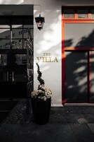 Entrada de um edifício com uma placa indicando “THE VILLA” e um vaso de planta em frente.