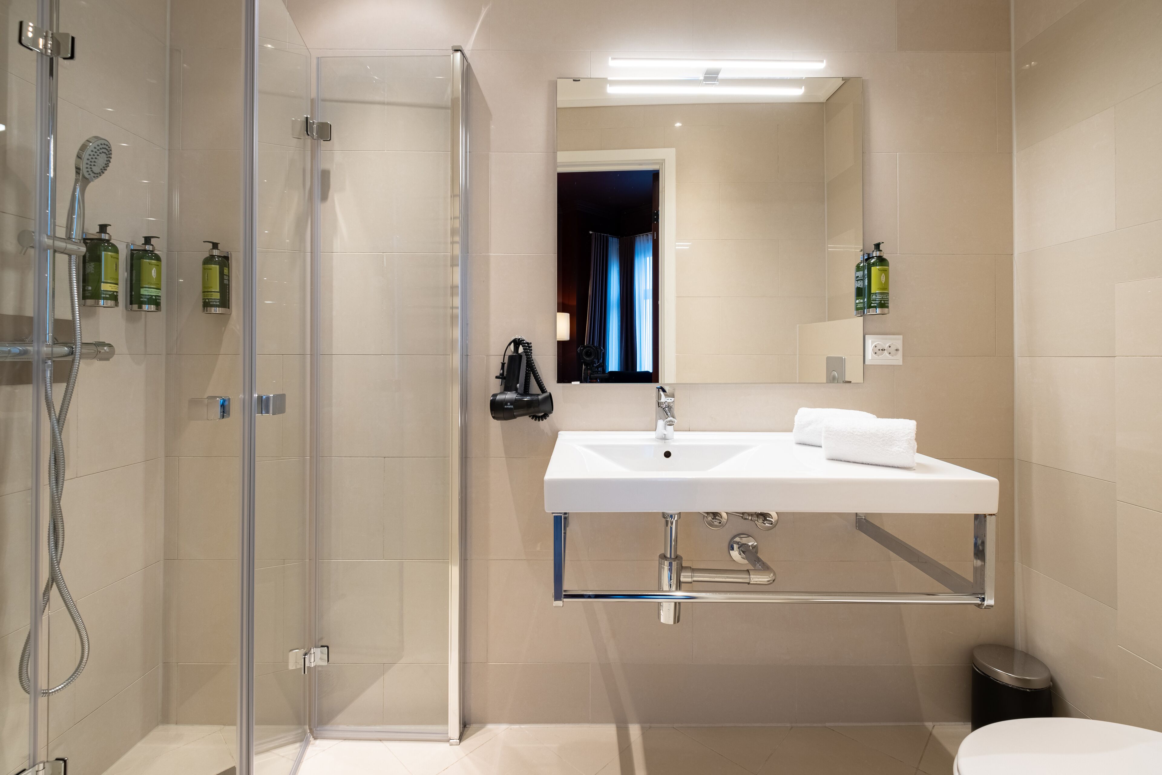 A modern bathroom with a glass shower enclosure, a white sink with a mirror above, and toiletries on the wall.