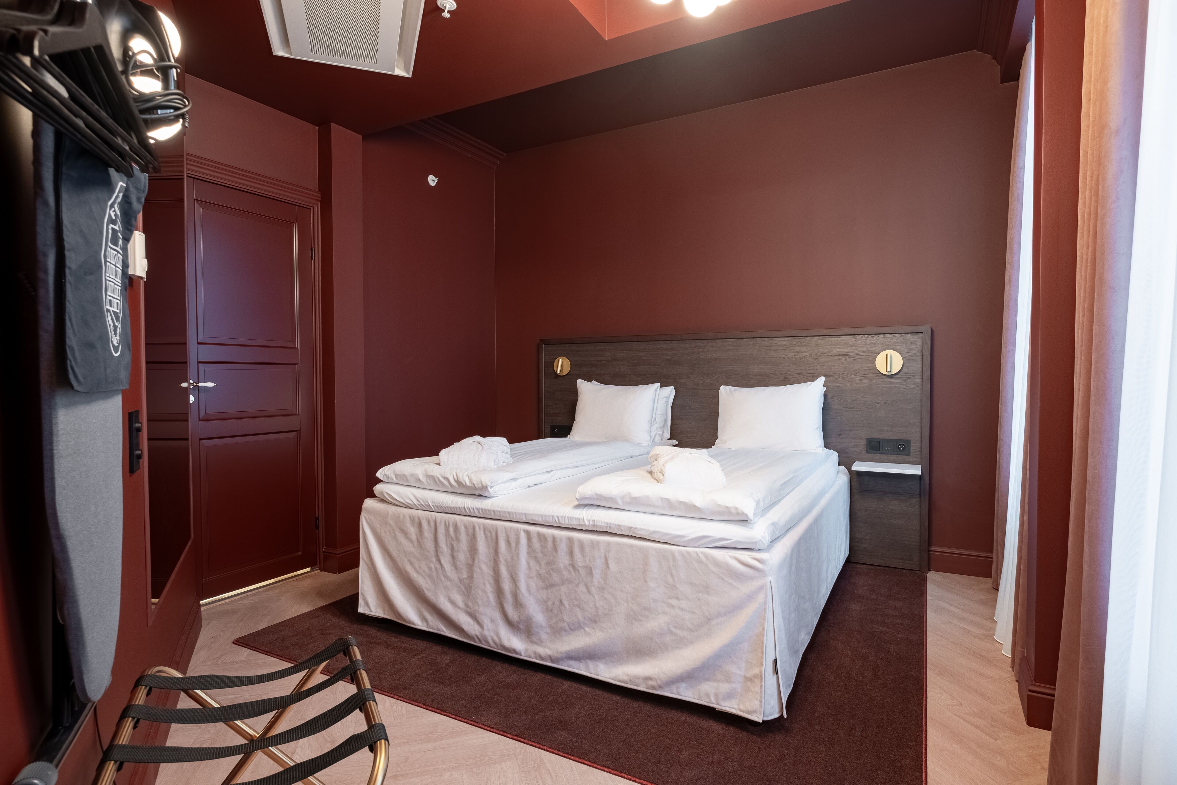 A neatly made bed with white linens and pillows, a wooden headboard, and a dark brown wall.