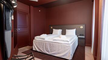 A neatly made bed with white linens and pillows, a wooden headboard, and a dark brown wall.