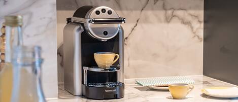 A modern kitchen with a built-in Nespresso coffee machine, marble backsplash, and a breakfast setting with croissants and glasses.