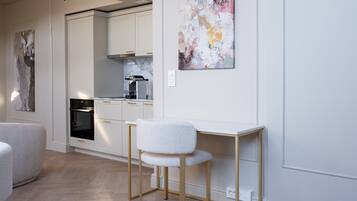 A modern kitchen with white cabinetry, a built-in oven, and a white chair at a wooden desk.