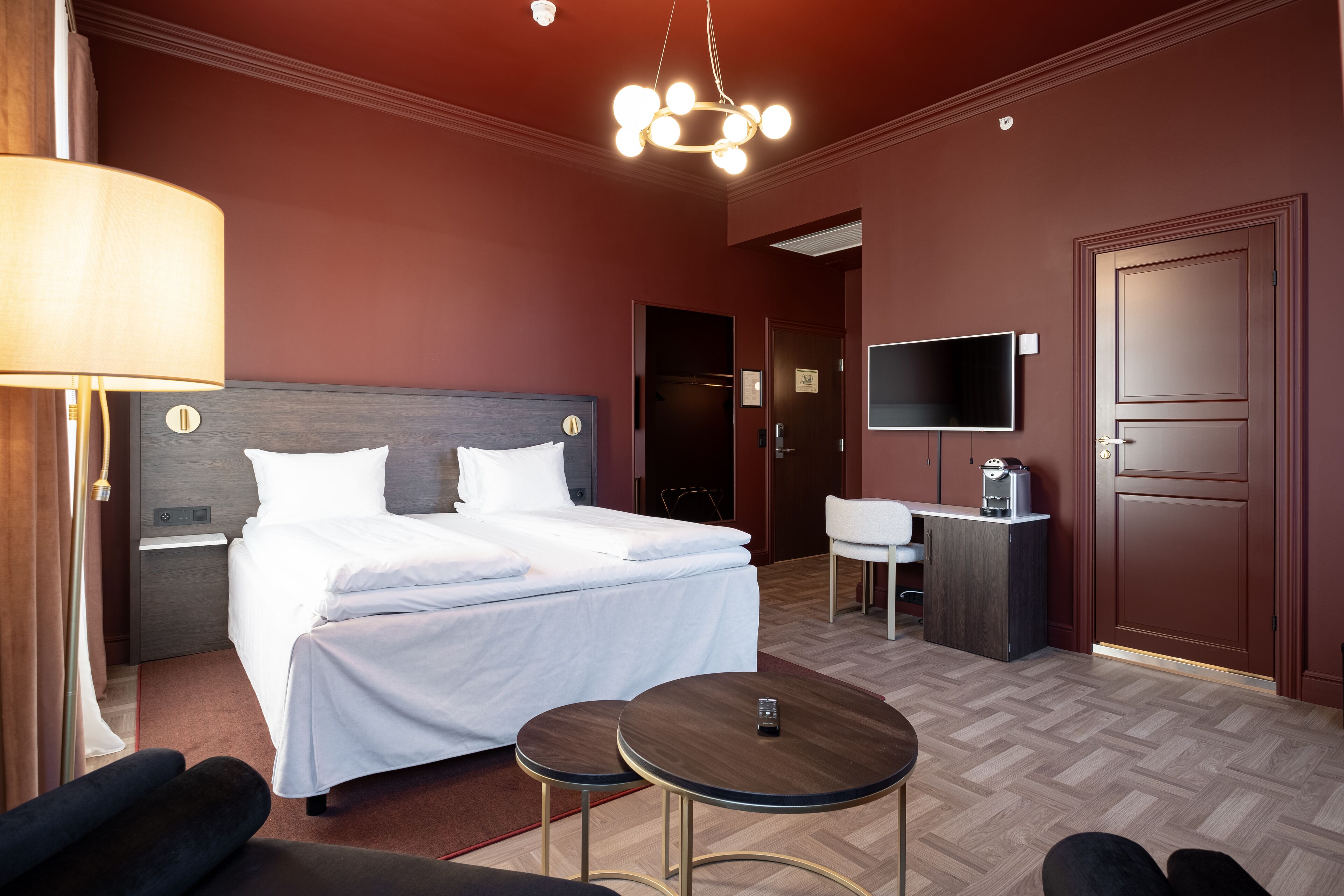 A hotel room with a large bed, bedside tables, a desk with a chair, a TV, and a small round table.