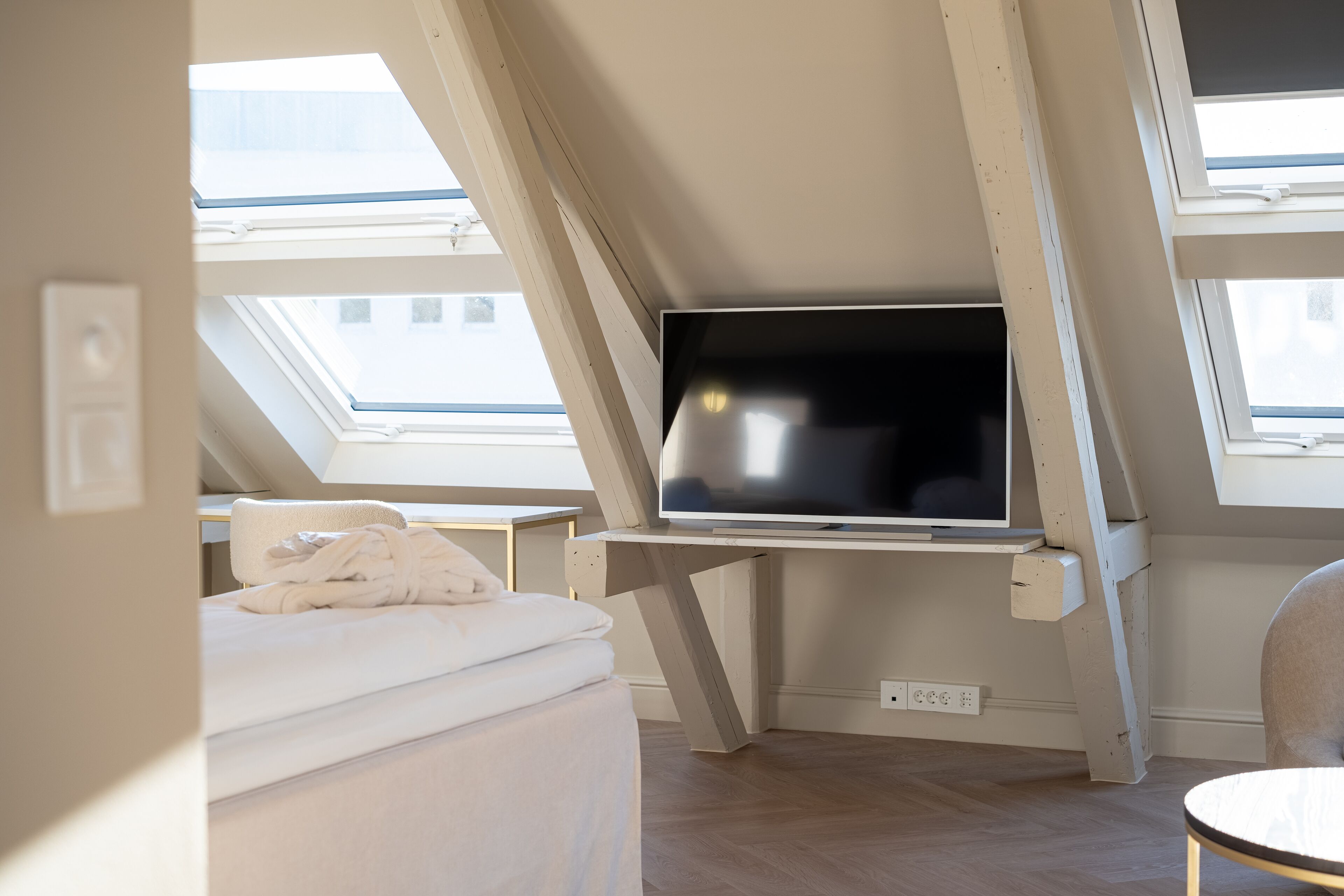 A bedroom with a skylight, a bed, a TV on a stand, and a chair.