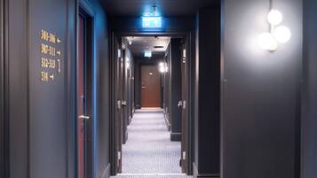 A hotel hallway with numbered doors, an exit sign, and a patterned carpet.