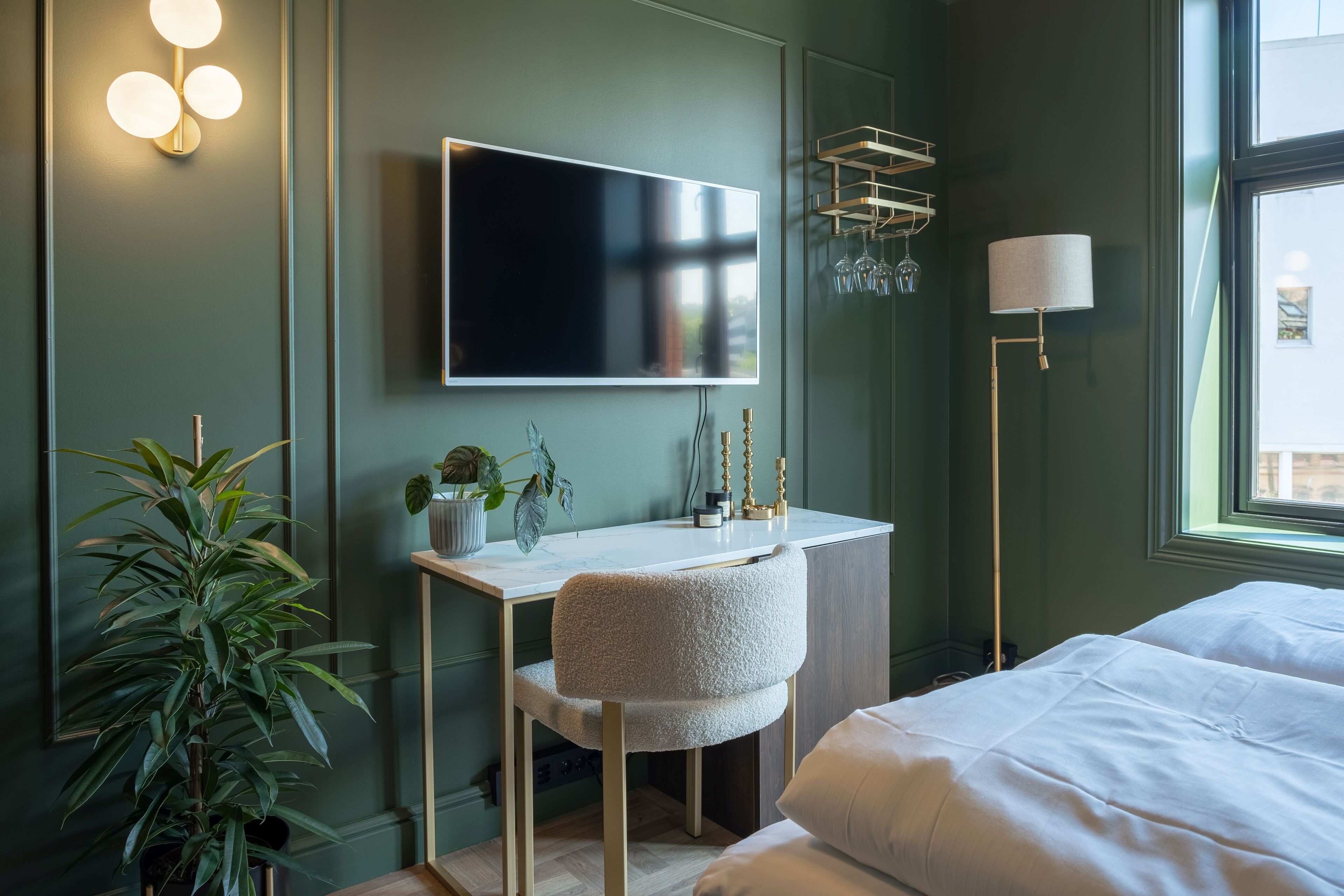 Une chambre moderne avec un lit, un bureau et un téléviseur. On y trouve également une plante et une lampe.