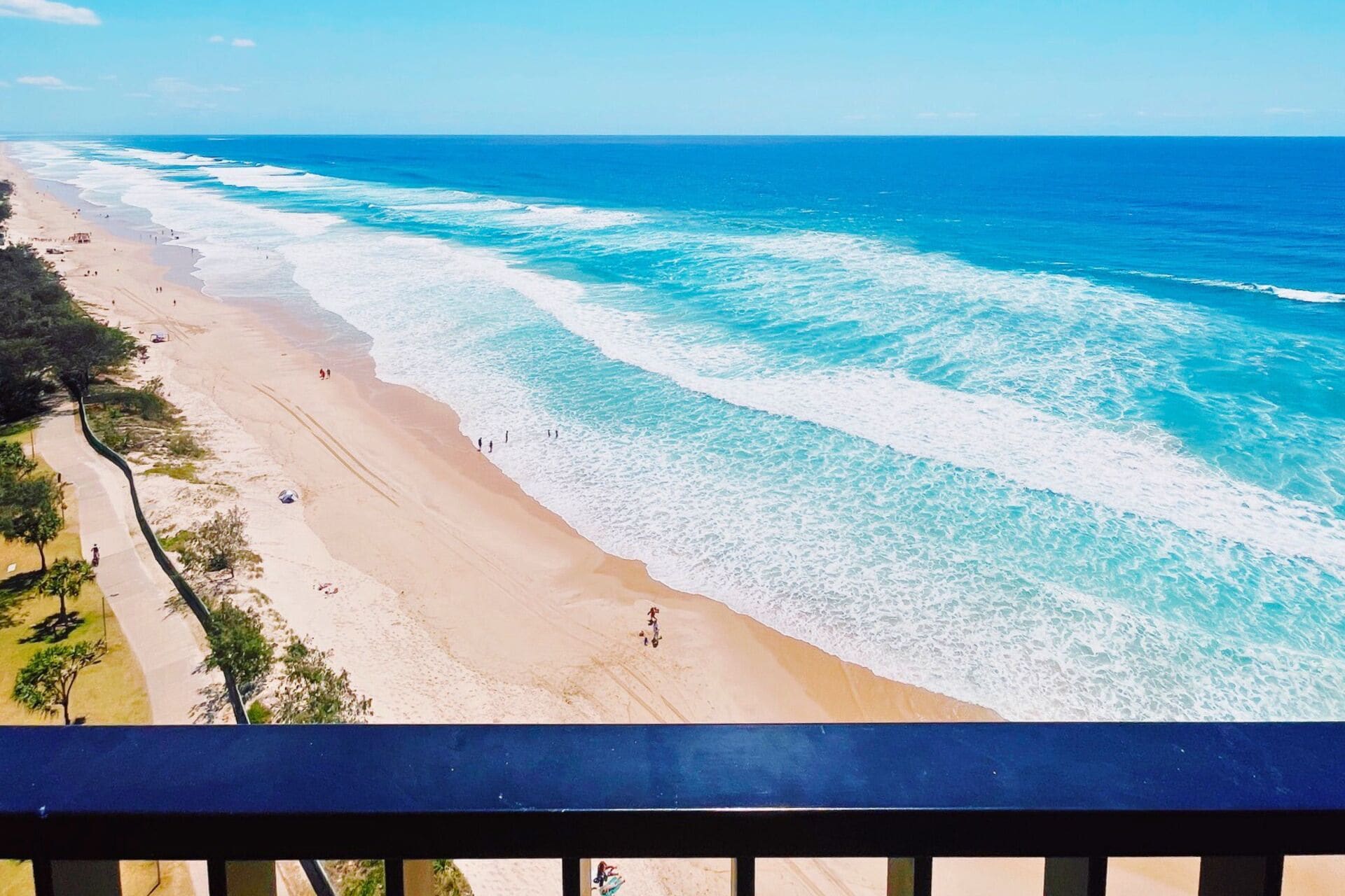 A beach with a clear view of the ocean, a sandy shore, and a few people walking along the beach.