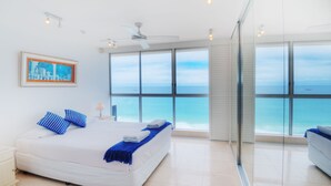 A bedroom with a large bed, a ceiling fan, and a view of the ocean through large windows.