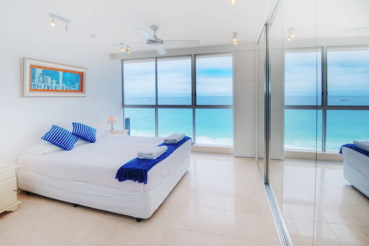 A bedroom with a large bed, a ceiling fan, and a view of the ocean through large windows.