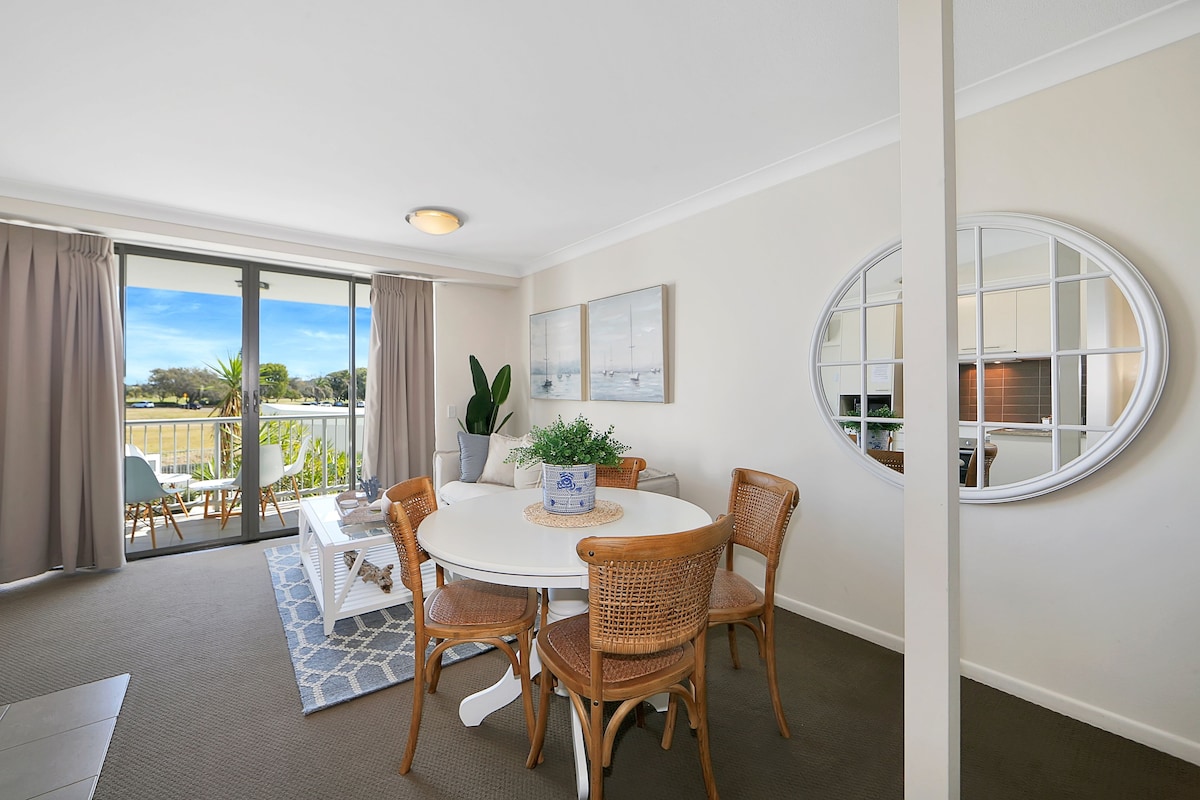 A dining area with a round table, four wicker chairs, a potted plant, and a view of the outdoors through a sliding door.