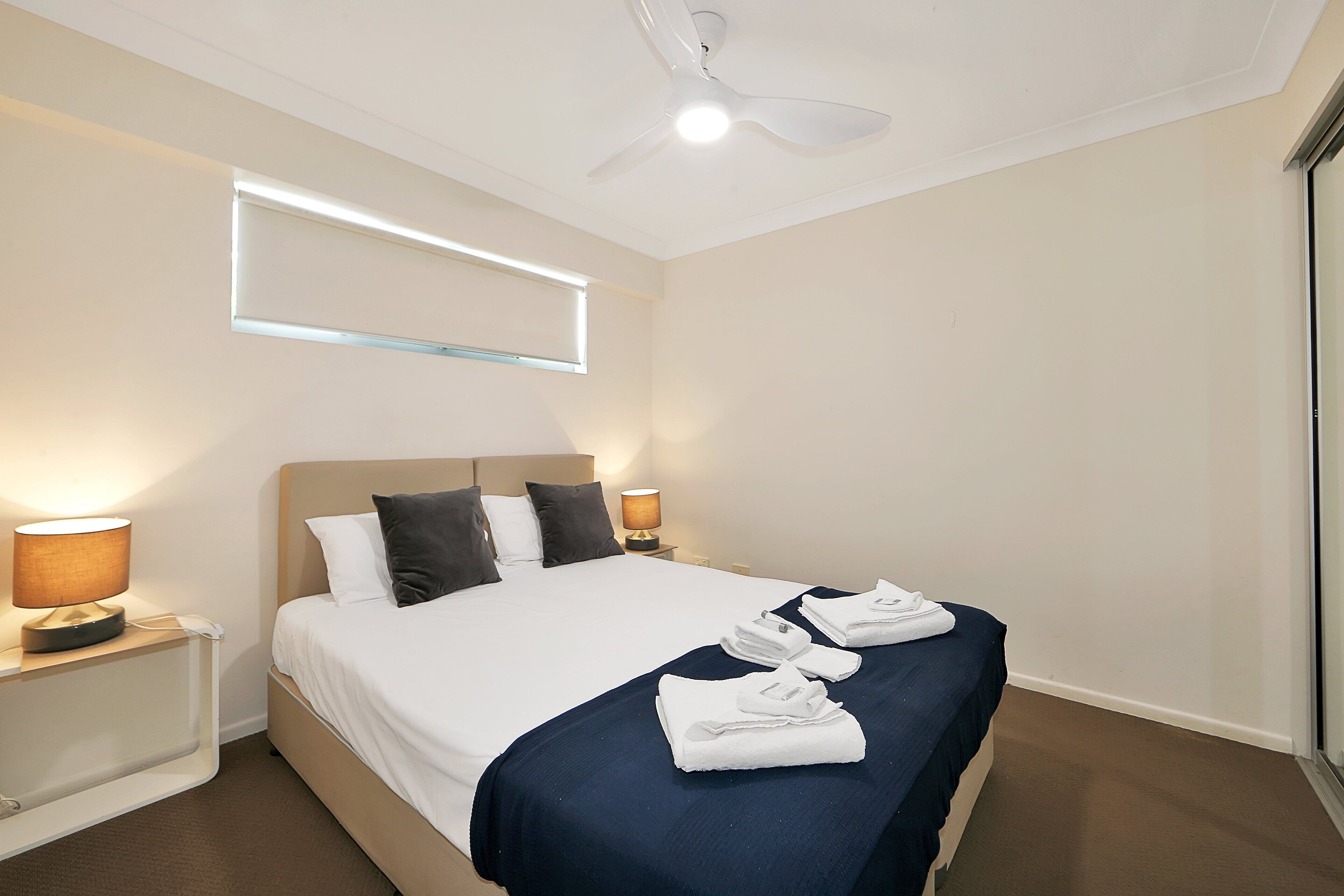 A hotel room with a bed, two bedside lamps, a ceiling fan, and a window with blinds.