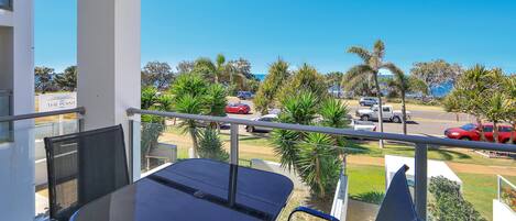 A balcony with a table and chairs, overlooking a parking area and greenery.