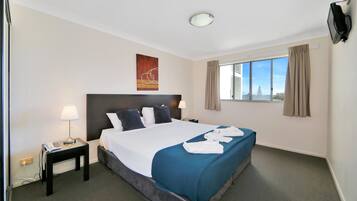 A hotel room with a bed, a nightstand, a lamp, a TV, and a window with curtains.