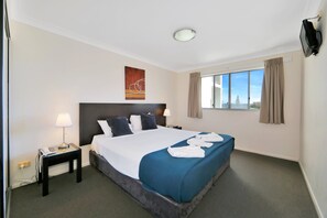 A hotel room with a bed, a nightstand, a lamp, a TV, and a window with curtains.