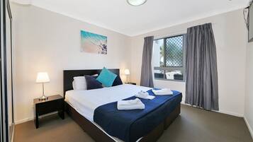 A neatly made bed with a blue bedspread, two pillows, and a small bedside table with a lamp.