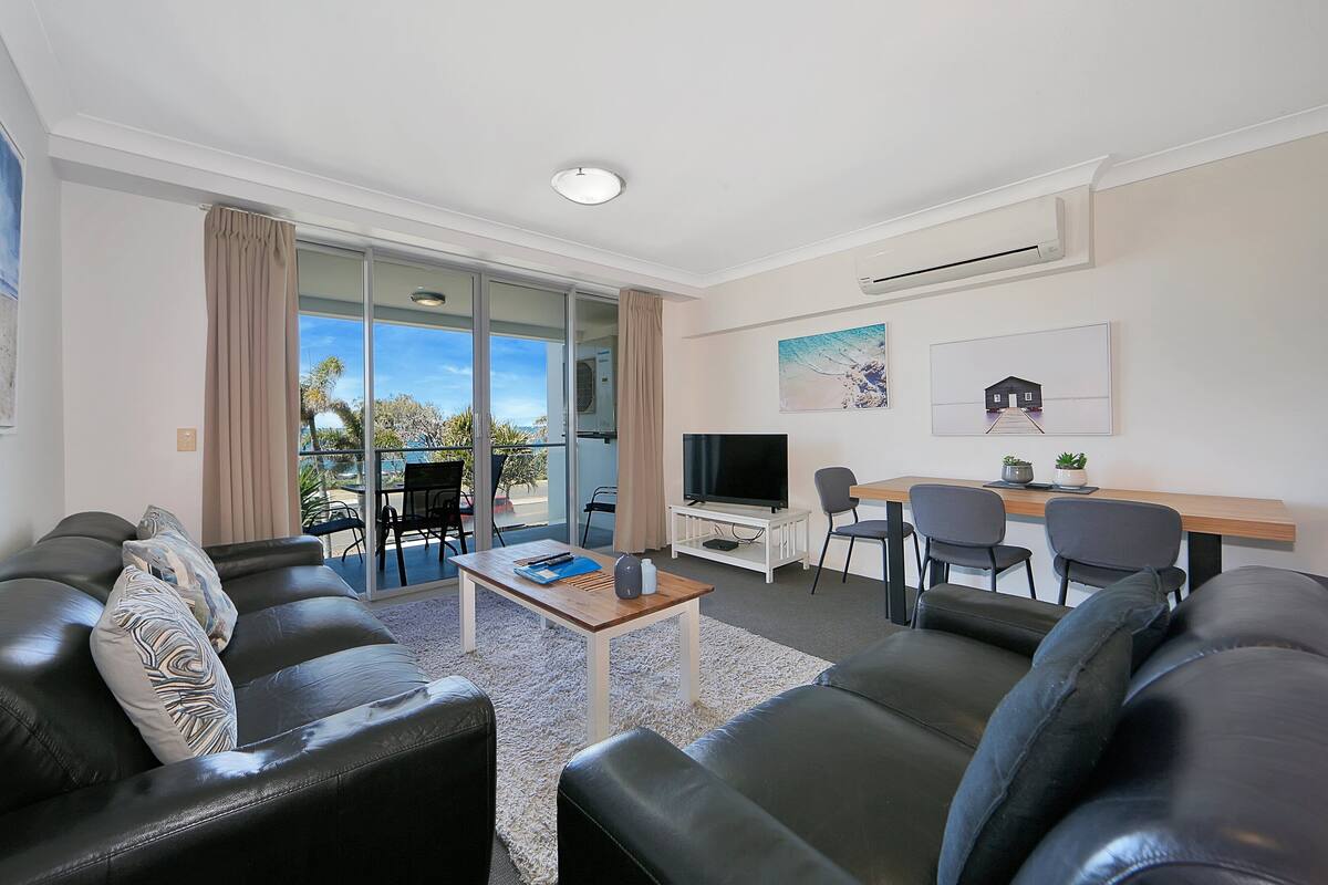 Uma sala de estar moderna com sofá, mesa de centro, televisão e área de jantar.