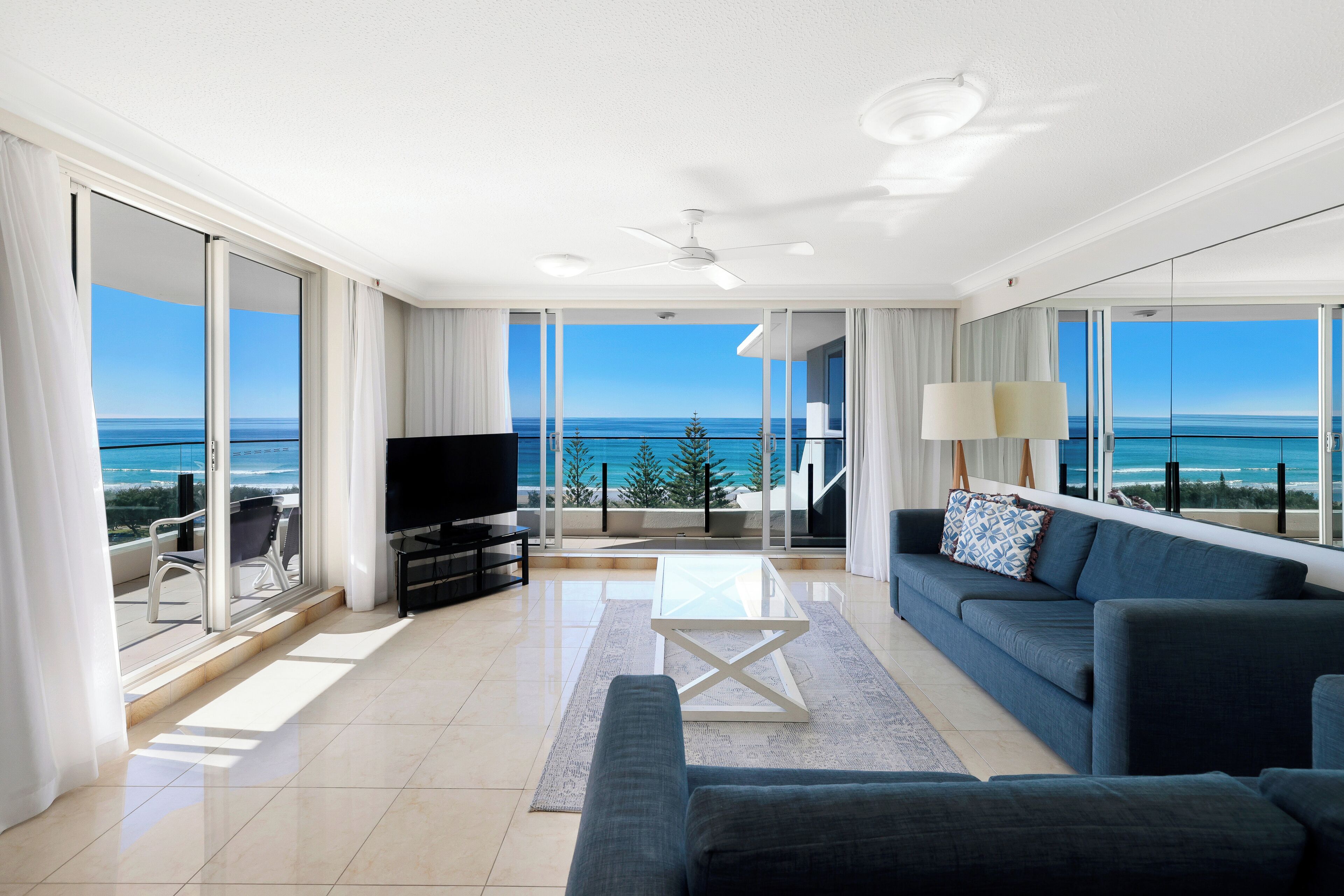 Un soggiorno moderno con una grande TV, un divano e un tavolino. C'è un balcone con vista sull'oceano.