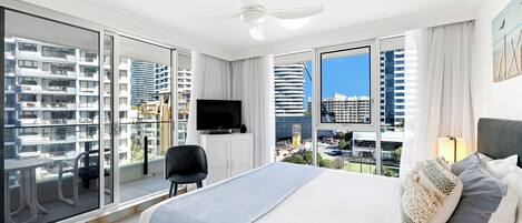 Una habitación de hotel moderna con una cama grande, un televisor de pantalla plana, un ventilador de techo y un balcón con vistas a la ciudad.