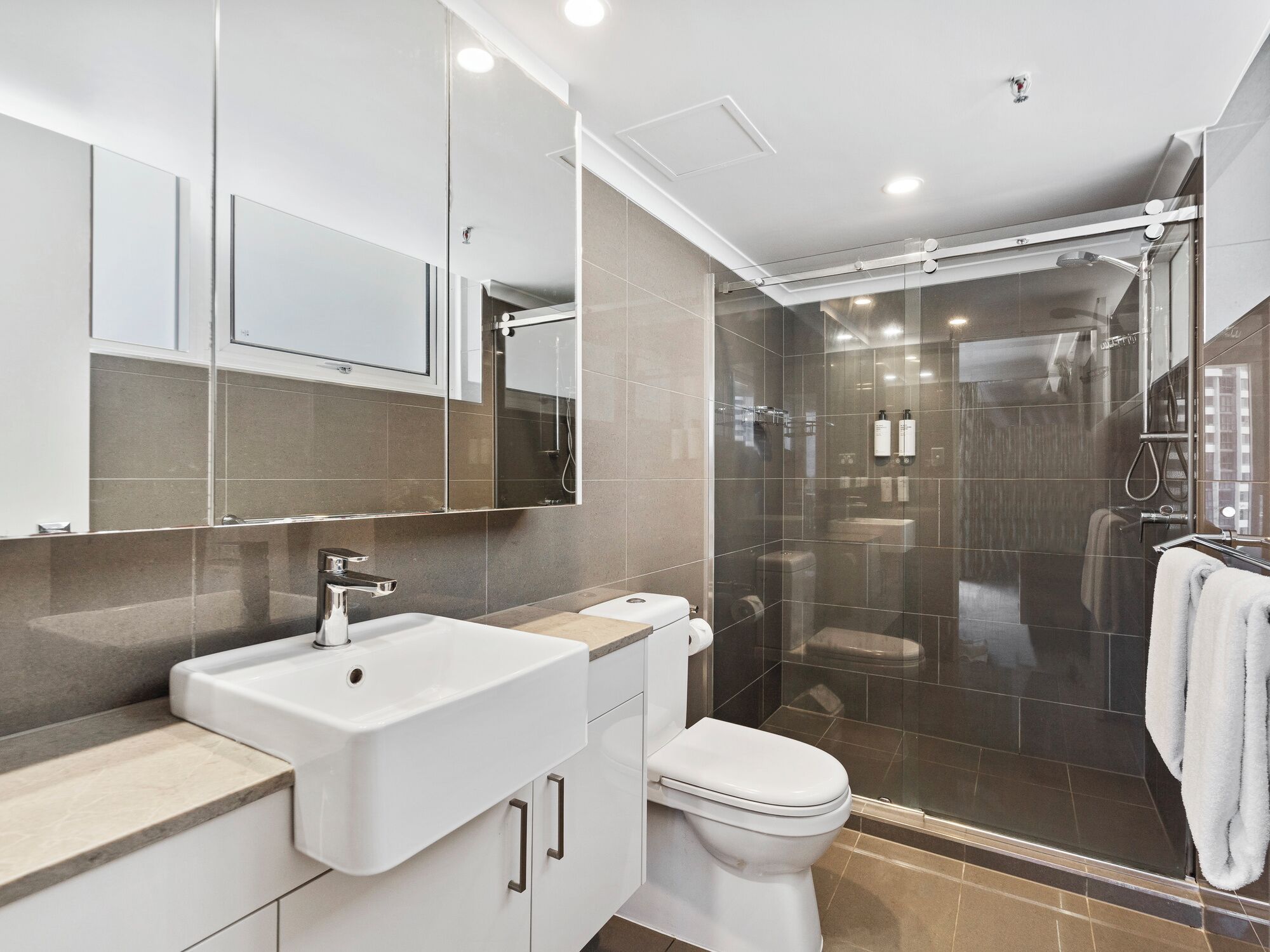 Un baño moderno con ducha de vidrio, lavamanos blanco y retrete.