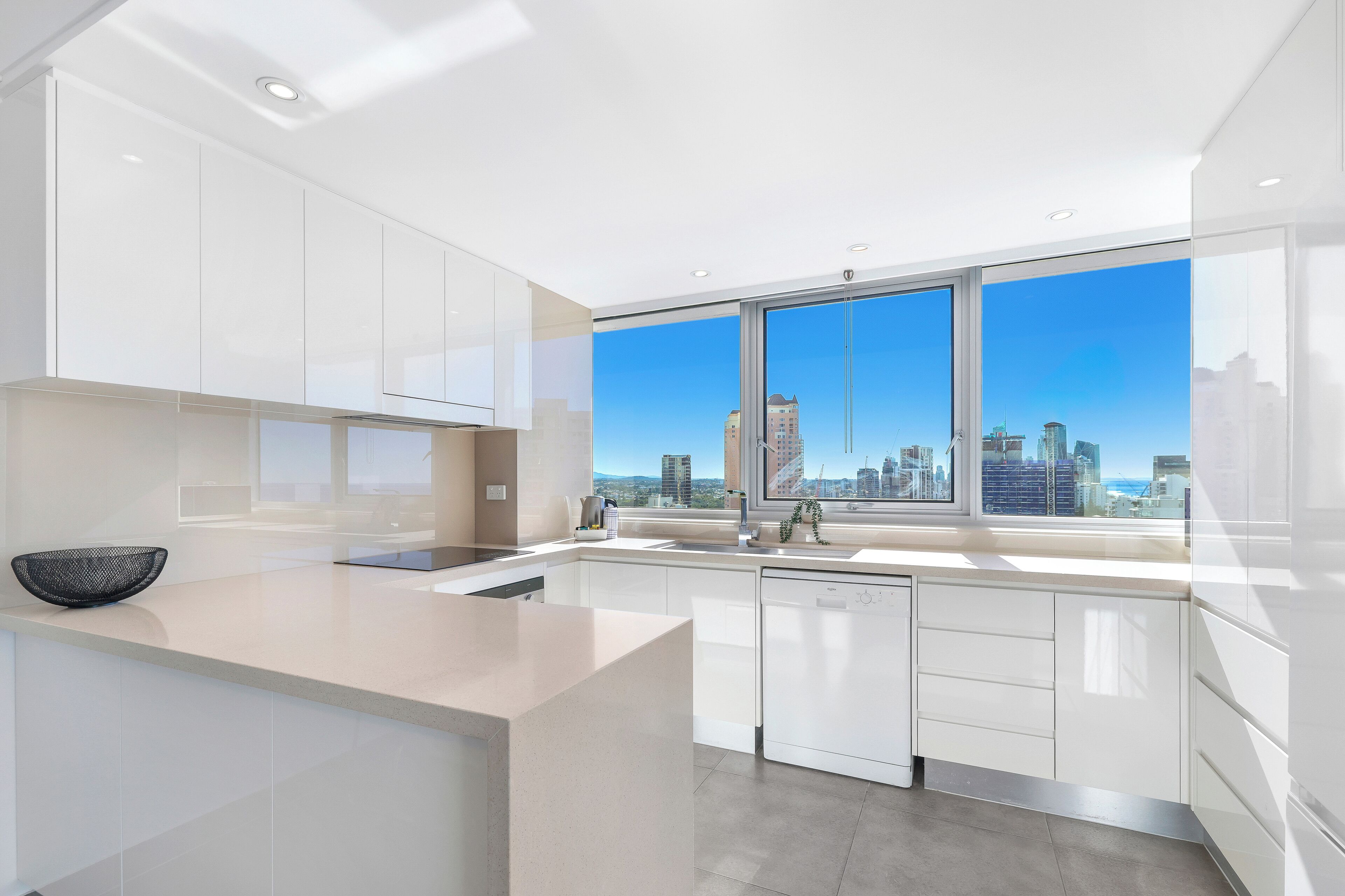 A modern kitchen with white cabinetry, a large window with a city view, and a kitchen island.