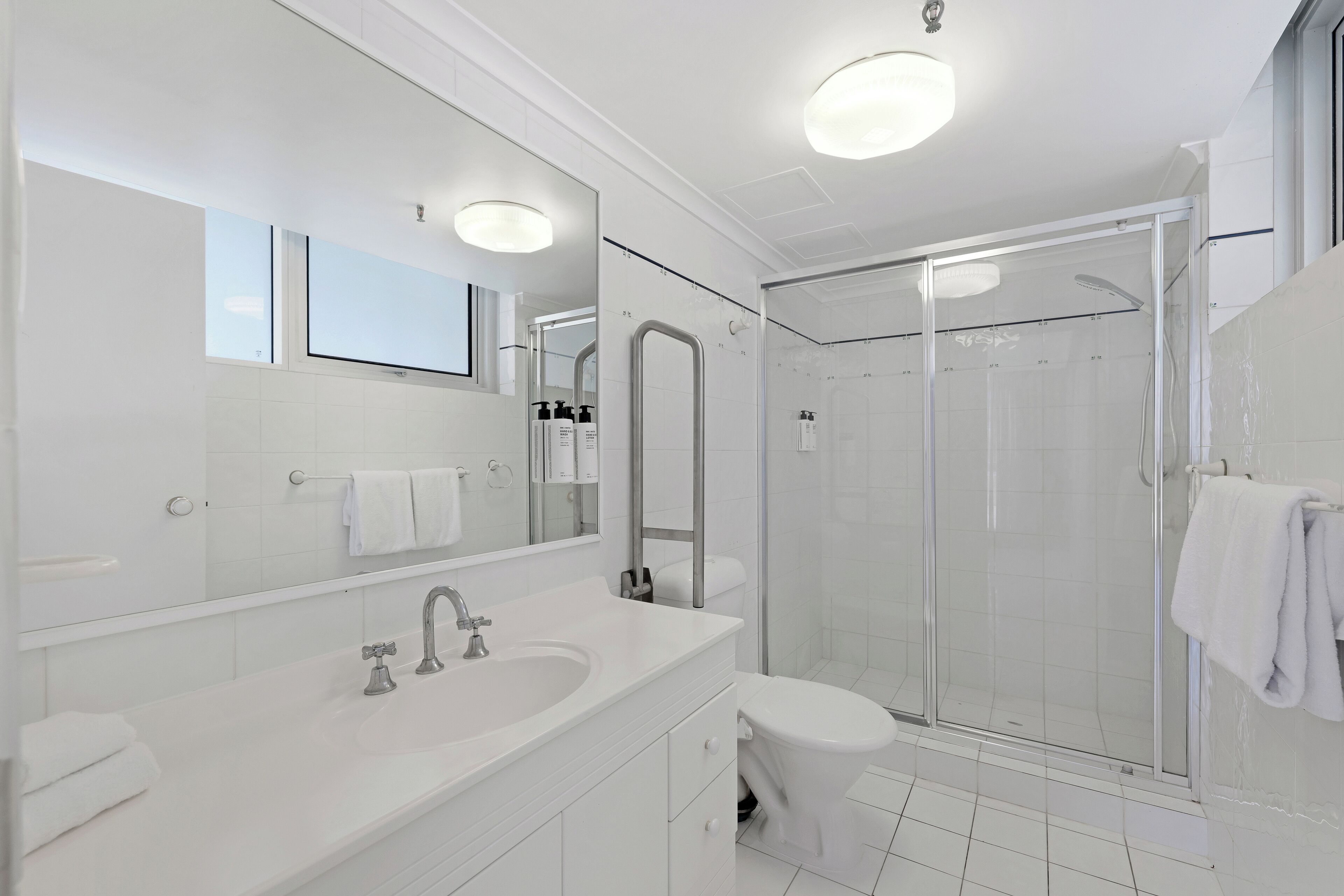 Un baño moderno con un espejo grande, un lavamanos, un inodoro y una ducha con mampara de vidrio.