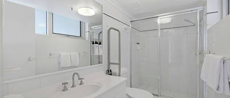 Un baño moderno con un espejo grande, un lavamanos, un inodoro y una ducha con mampara de vidrio.