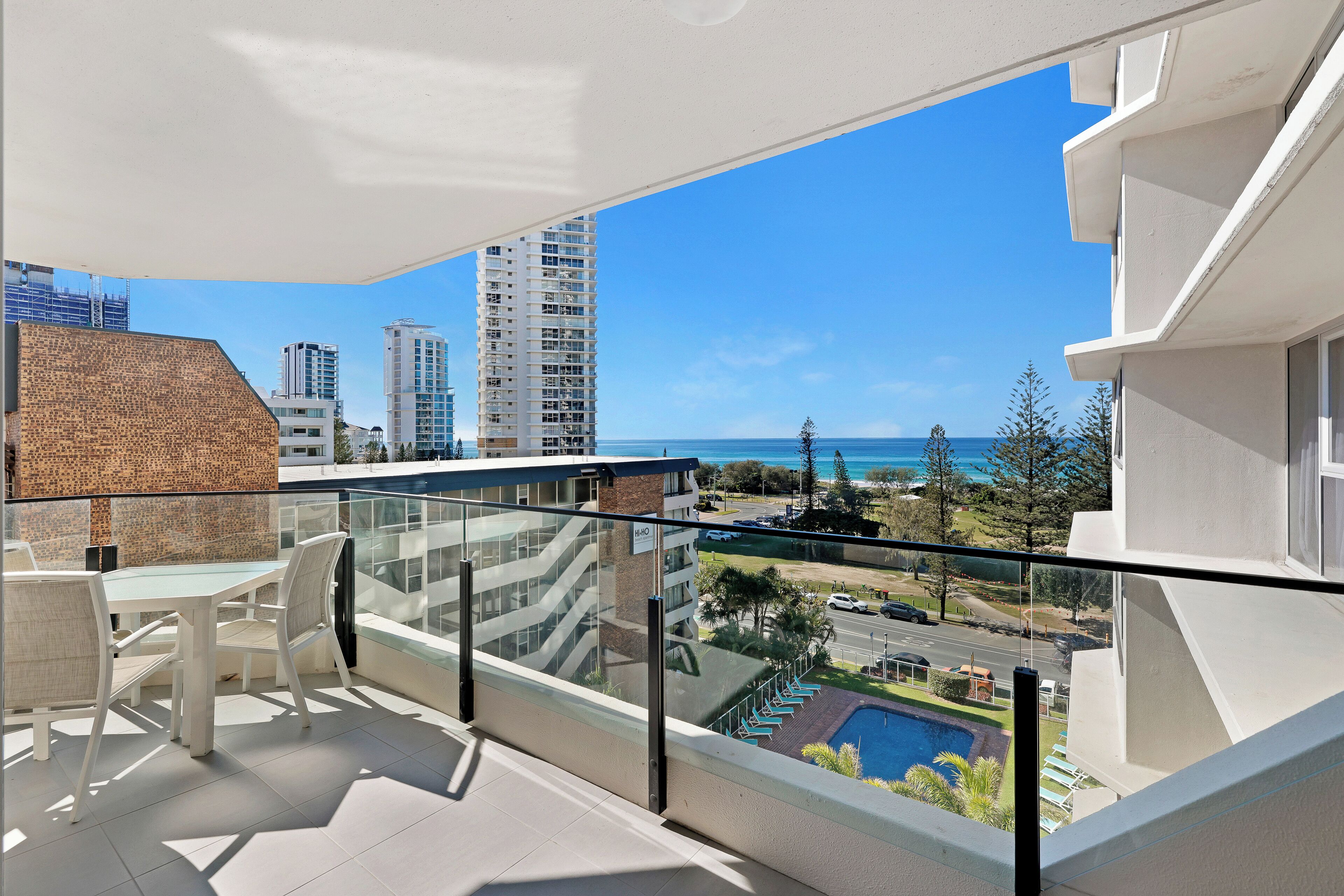 Ein Balkon mit Glasgeländer, ein Pool und Blick auf das Meer und Gebäude.