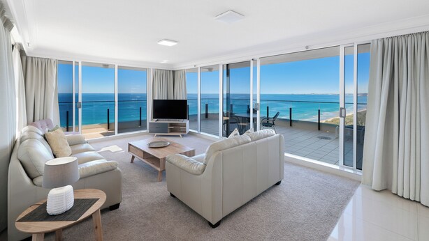 A spacious living room with a large window offering a view of the ocean, a flat-screen TV, and a comfortable seating area. - ULTIQA Beach Haven At Broadbeach (Broadbeach)