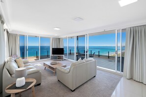 Amplia sala de estar con un ventanal que ofrece vistas al océano, un televisor de pantalla plana y una zona de estar confortable.
