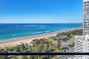 A coastal view from a high-rise building overlooking a beach with a parking area and a few buildings in the foreground.