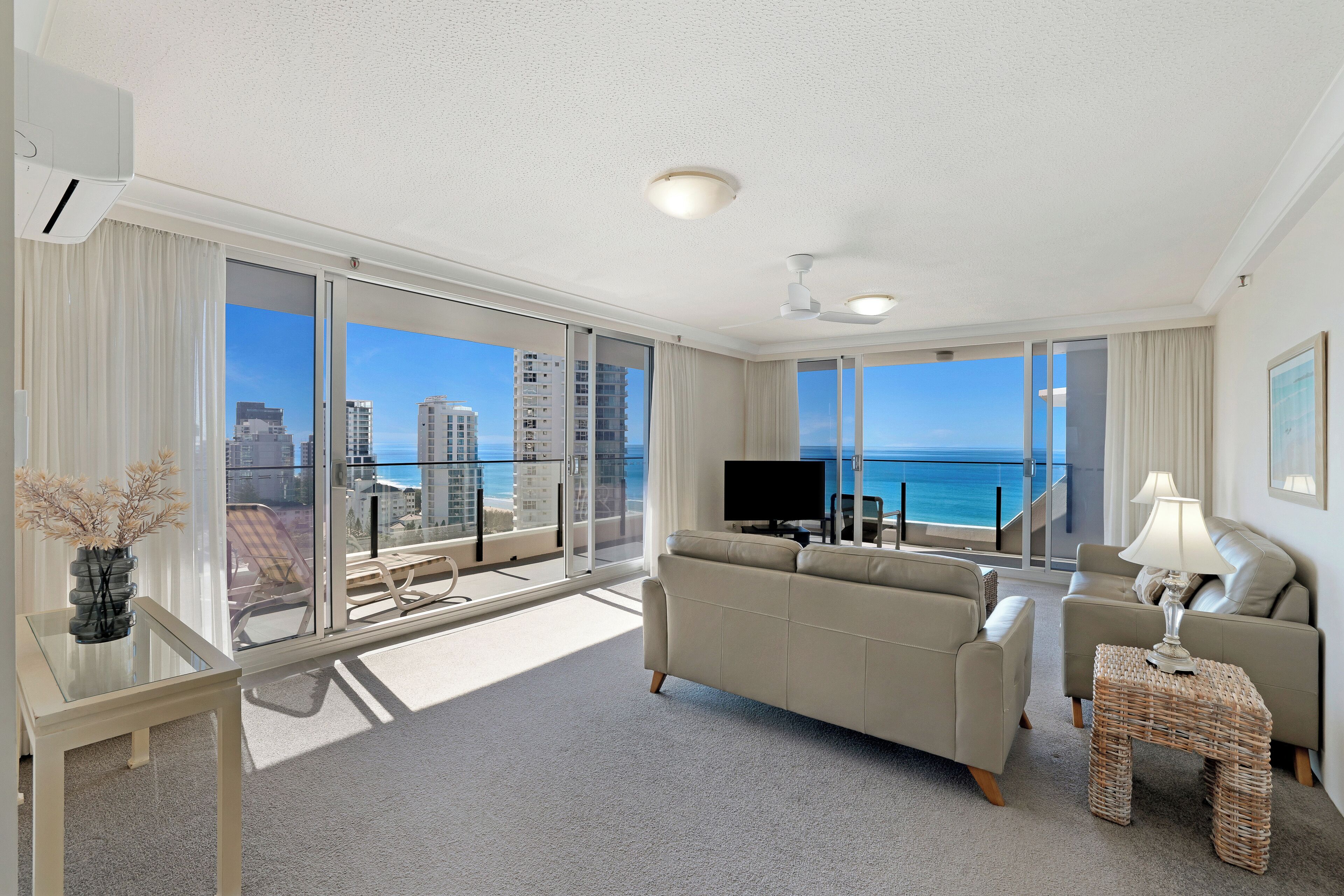 A spacious living room with a sofa, a TV, and a balcony with a view of the ocean.