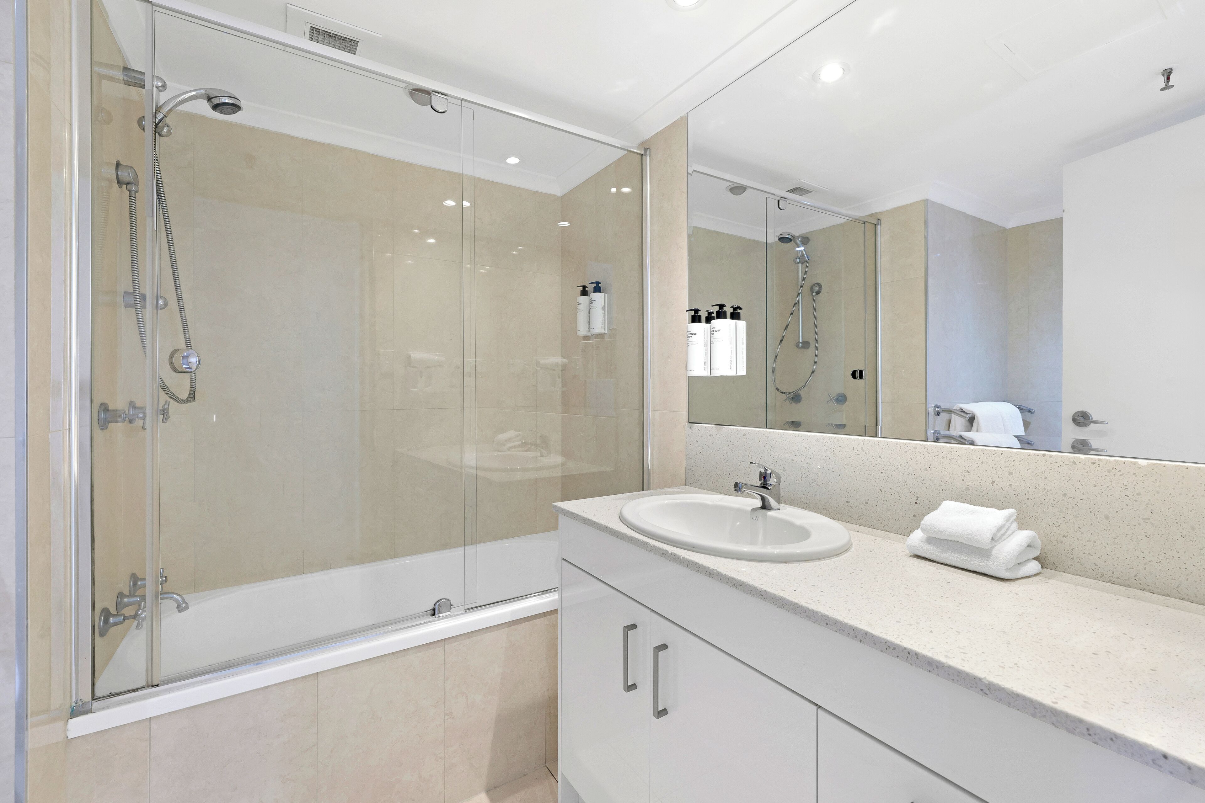 A modern bathroom with a glass-enclosed shower, a white sink, and a large mirror.