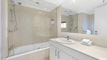 A modern bathroom with a glass-enclosed shower, a white sink, and a large mirror.