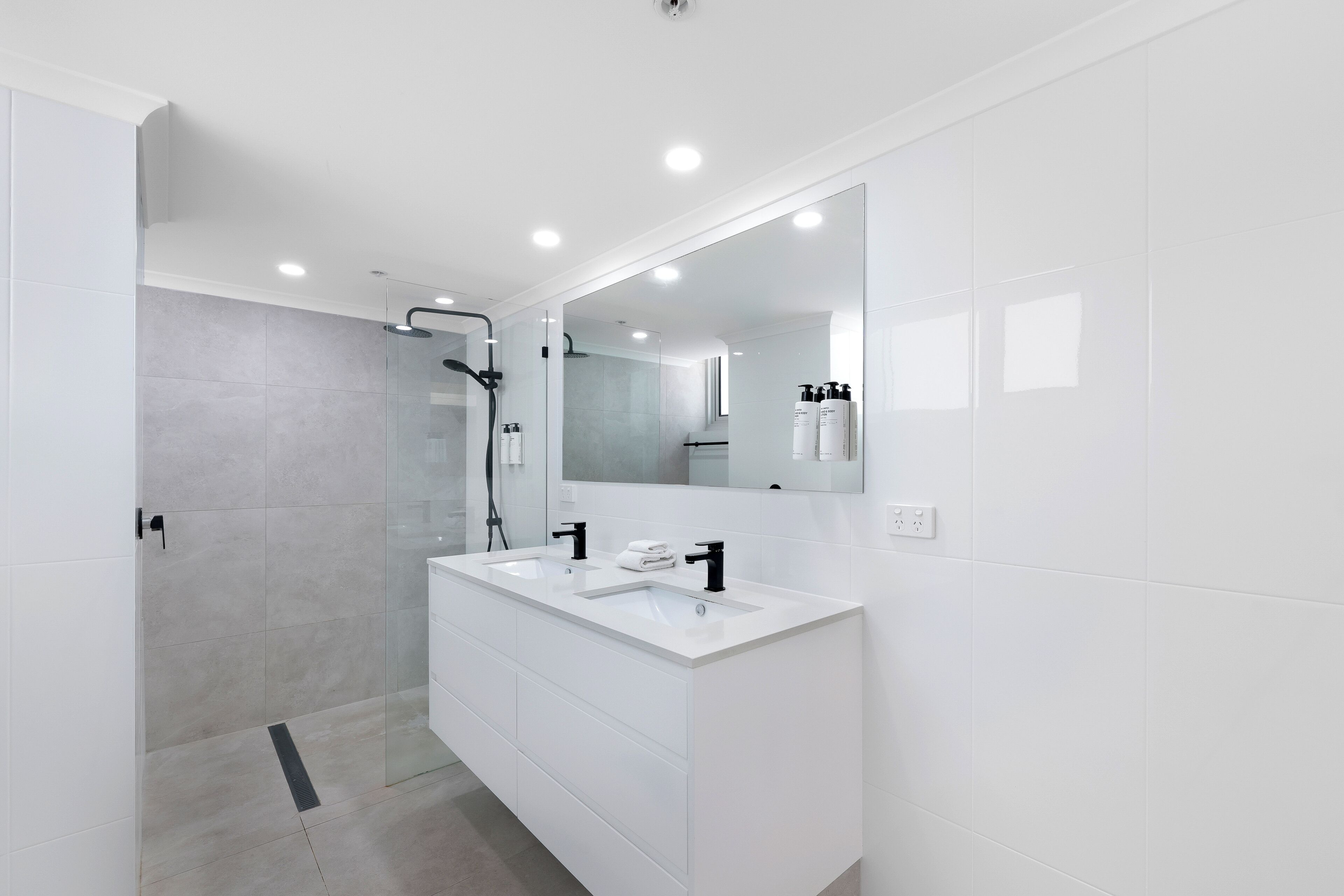 A modern bathroom with a glass-enclosed shower, a double sink vanity, and a large mirror.