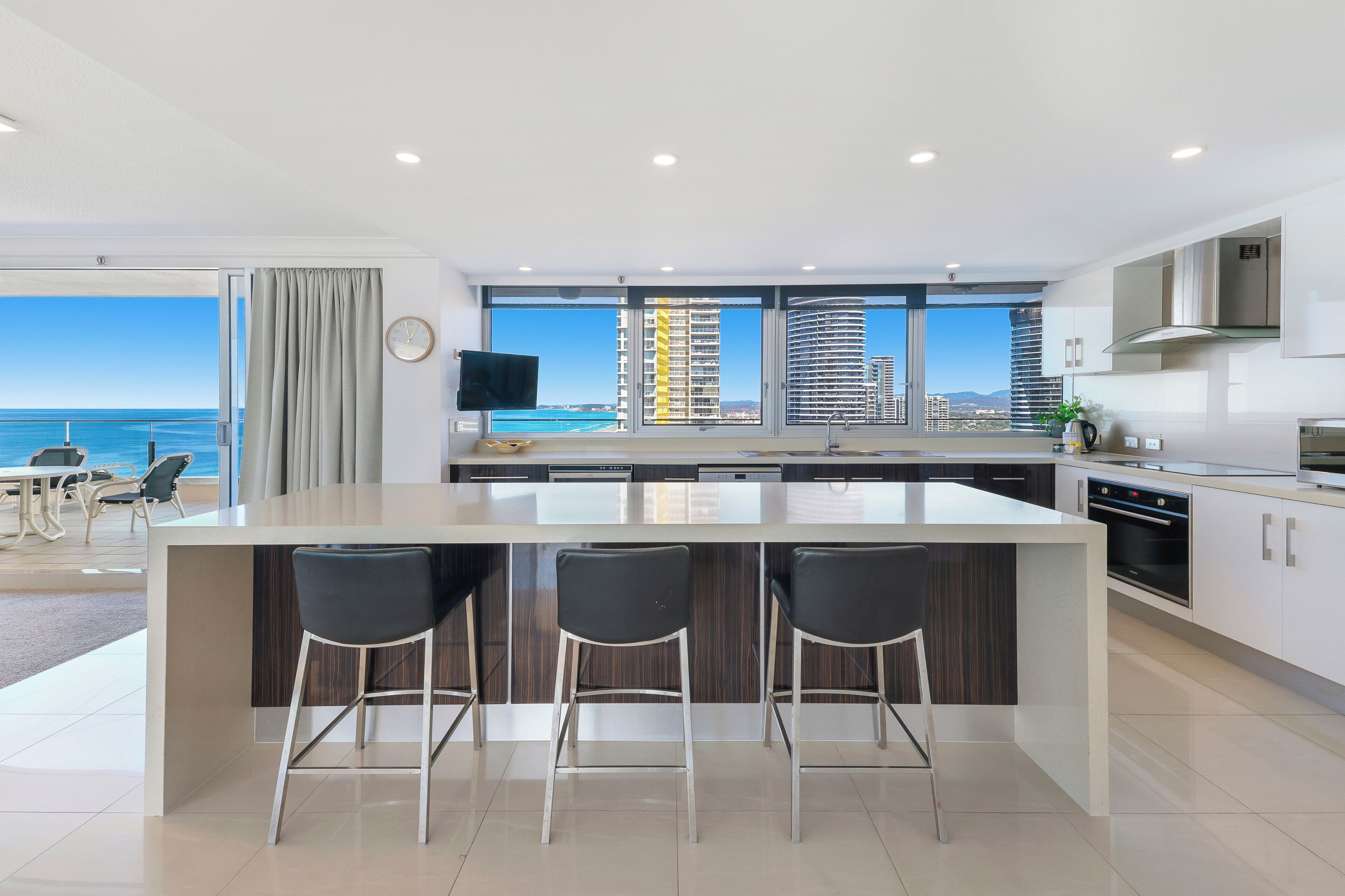 A modern kitchen with a large island, bar stools, and a view of the sea.