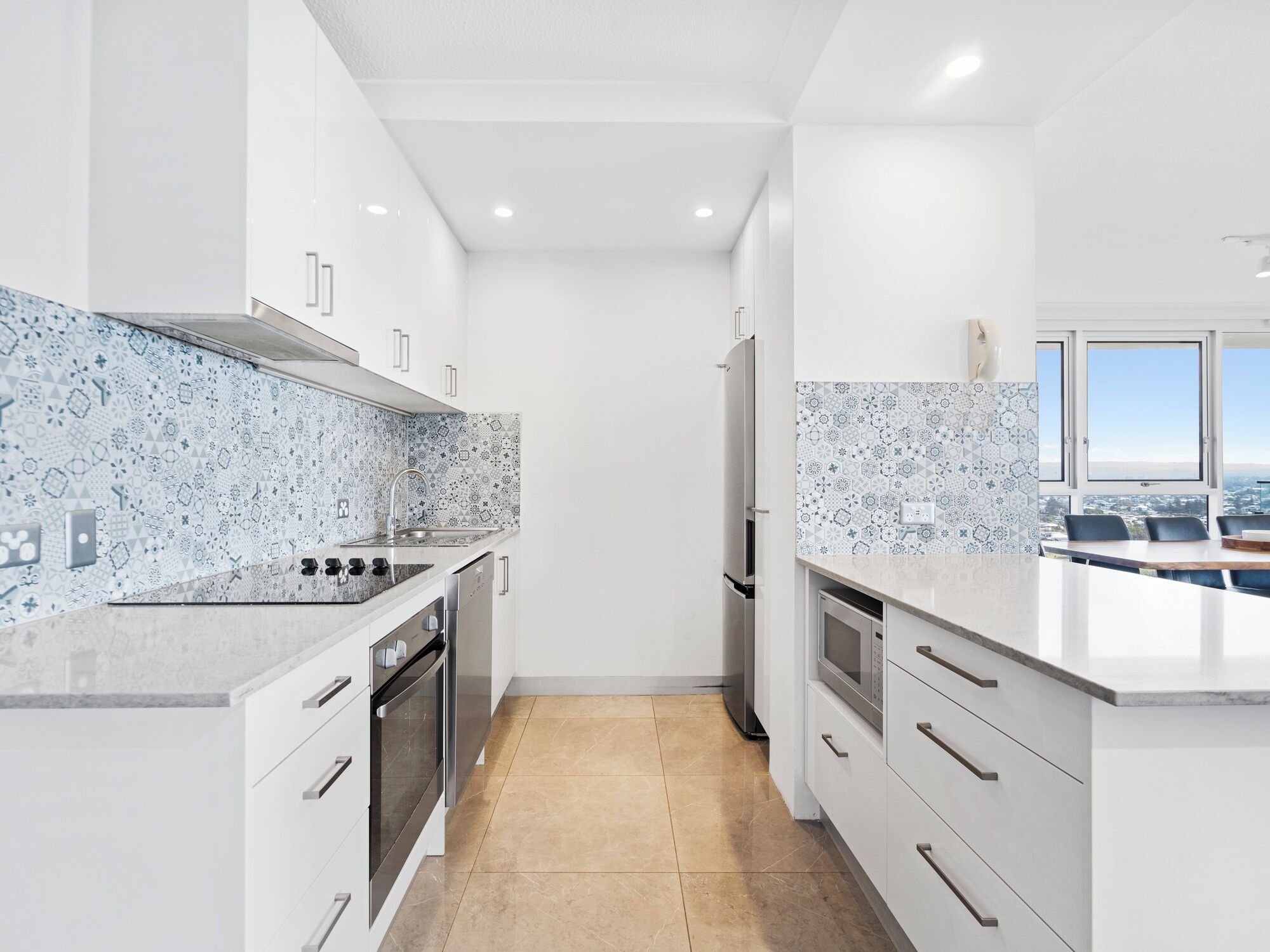 A modern kitchen with white cabinetry, a patterned backsplash, and a view of the city through large windows.