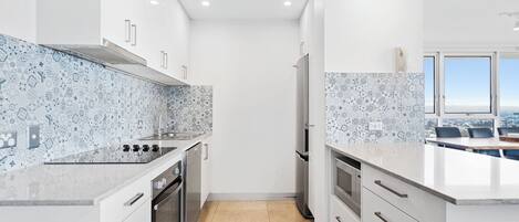 A modern kitchen with white cabinetry, a patterned backsplash, and a view of the city through large windows.