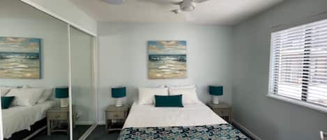 A bedroom with a bed, two bedside tables with lamps, a ceiling fan, and a large mirror.