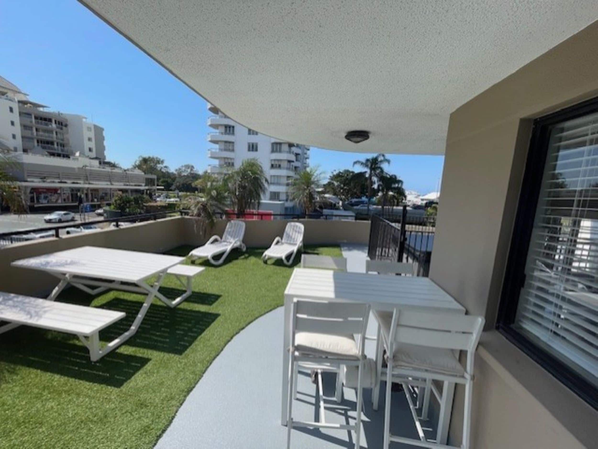 A balcony with a table and chairs, a small patch of artificial grass, and a view of the cityscape.