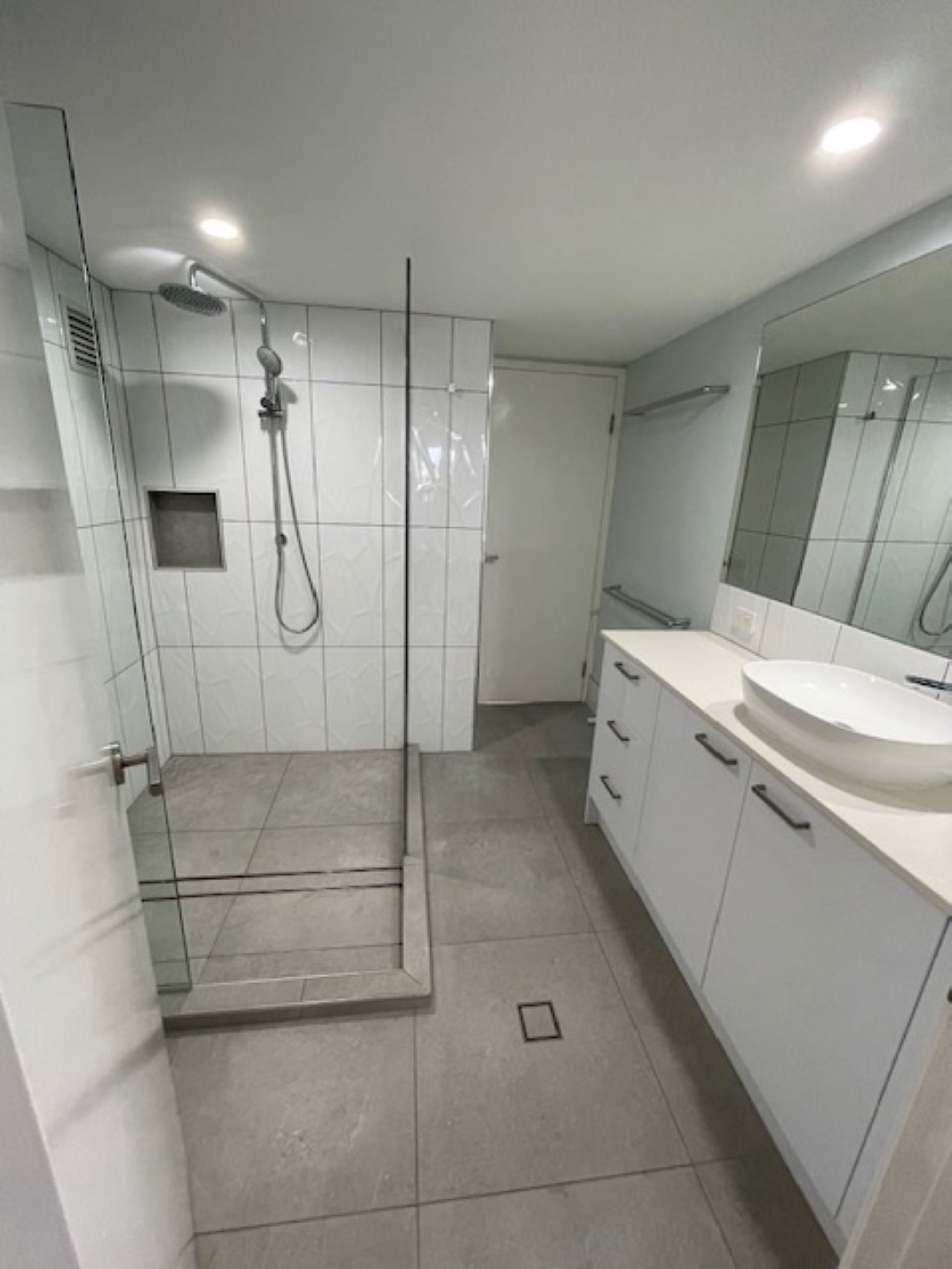 A modern bathroom with a glass-enclosed shower, a large mirror, and a white sink.