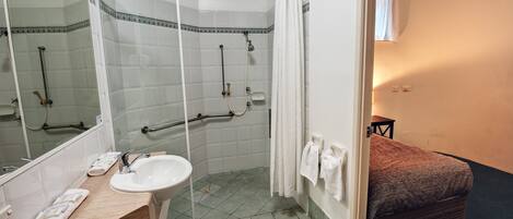 Un baño con ducha, lavamanos y una cama con manta.