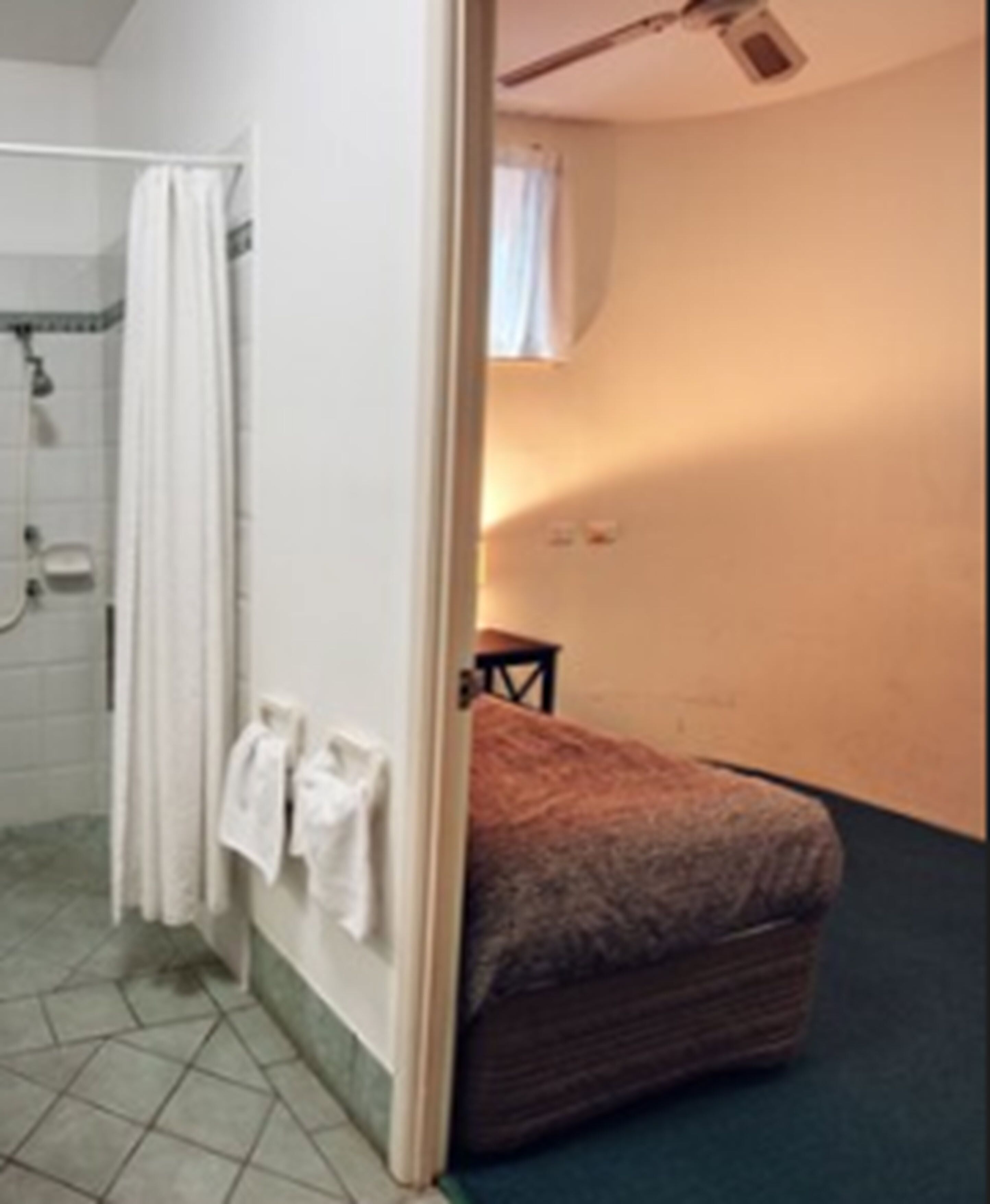 Casa de banho com chuveiro, um porta-toalhas e uma cama com colcha estampada.