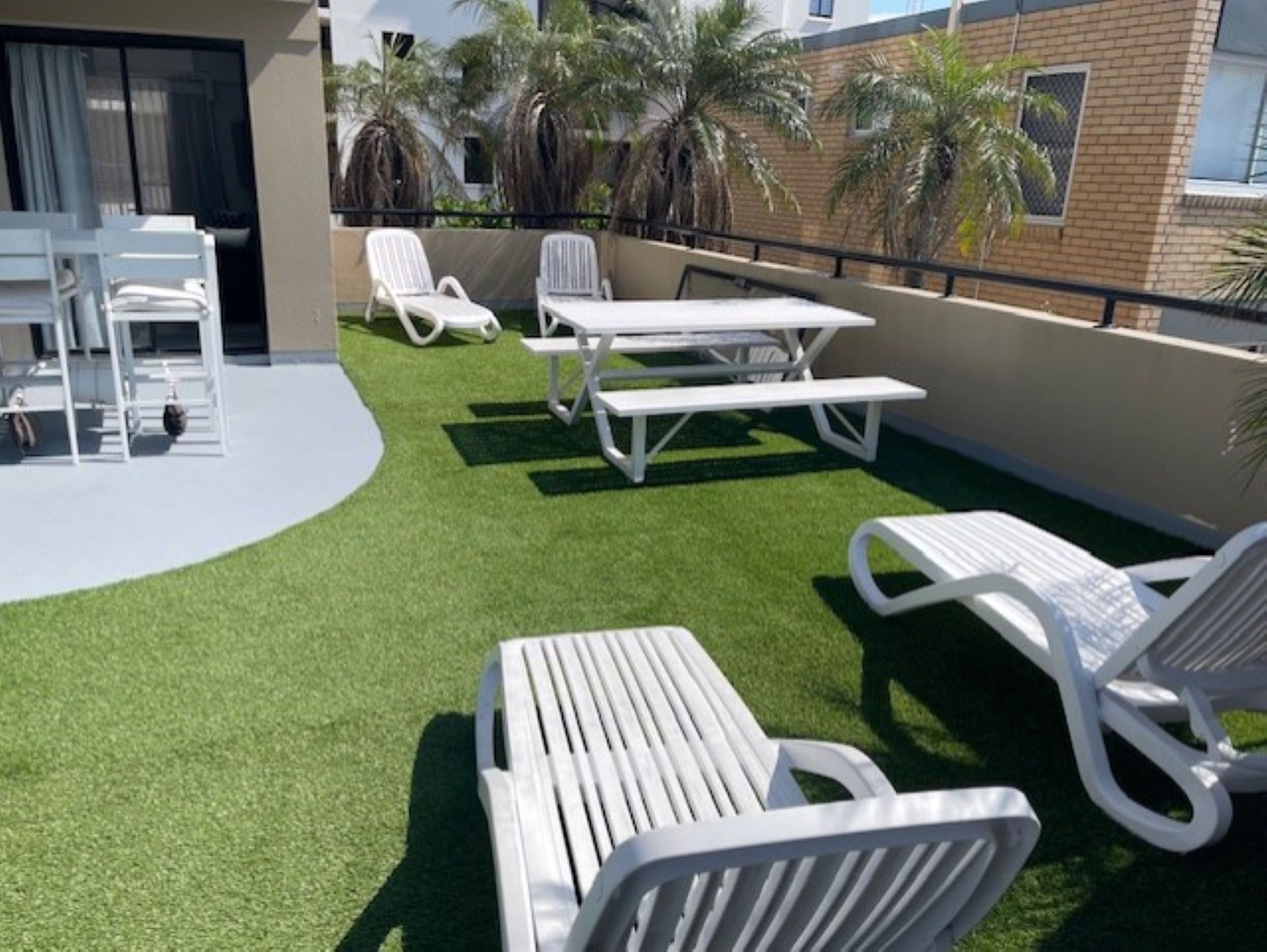 A rooftop terrace with artificial grass, white lounge chairs, and a picnic table.