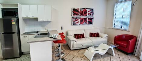 Un espacio habitable compacto con kitchenette, comedor, sofá y sillón rojo.