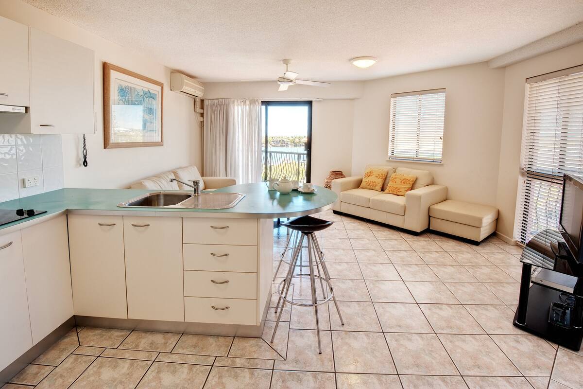A compact kitchen with a central island, a bar stool, a sofa, and a coffee machine.
