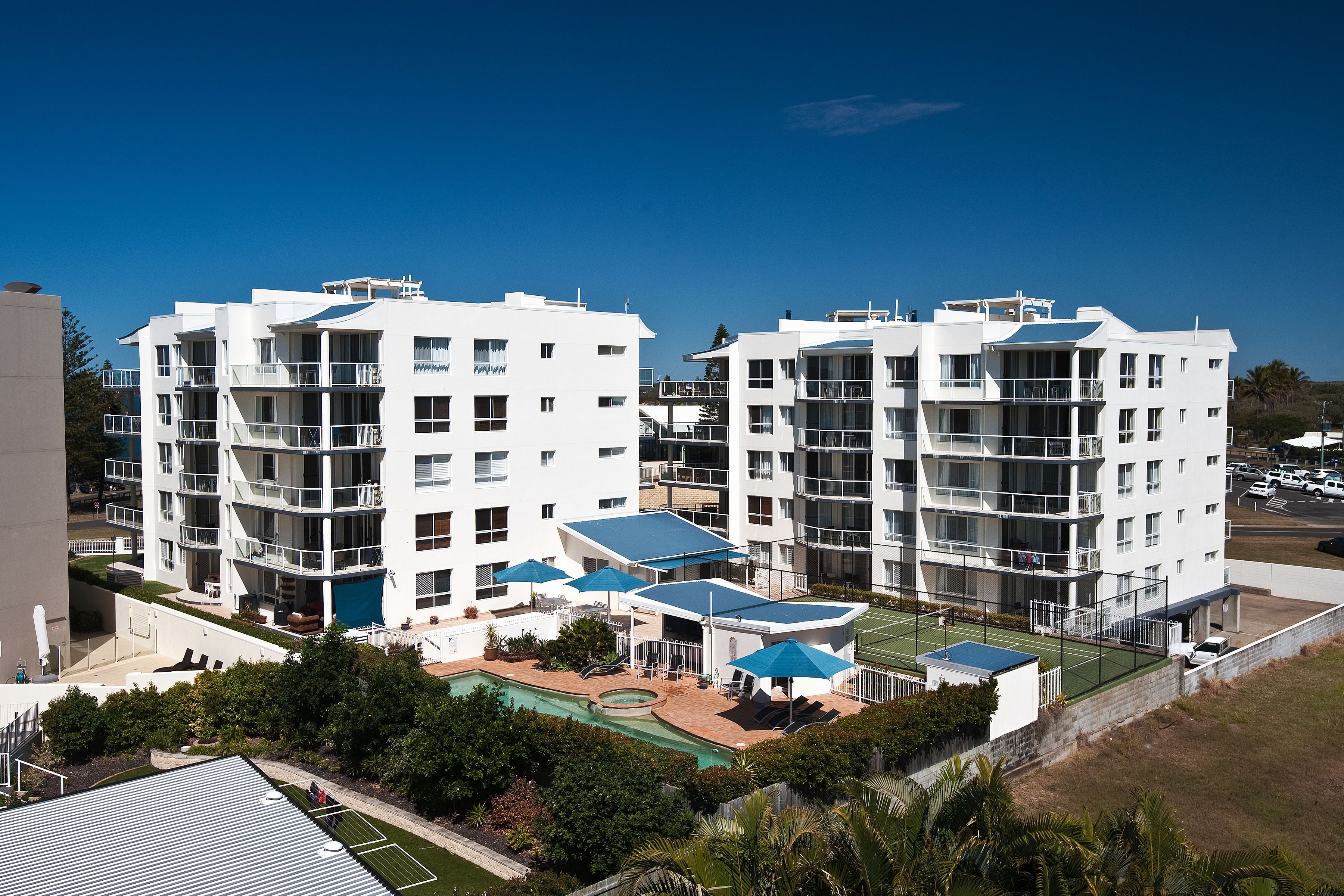A modern multi-story hotel with balconies, a pool area, and a tennis court.