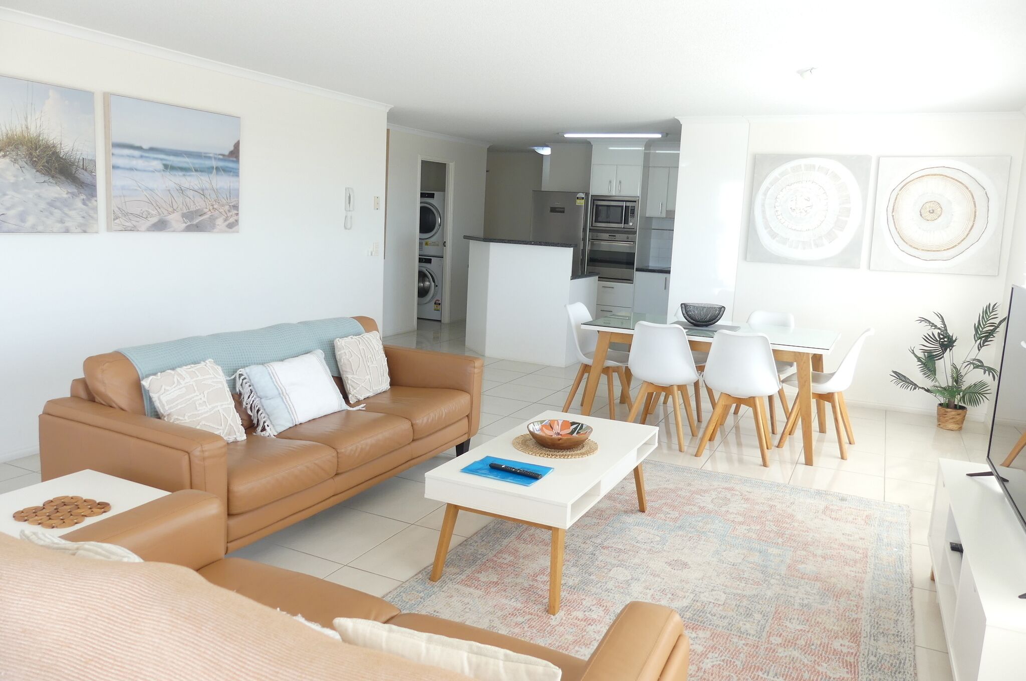 En moderne stue med en brun lædersofa, et hvidt sofabord og et spiseområde med hvide stole og et træbord.