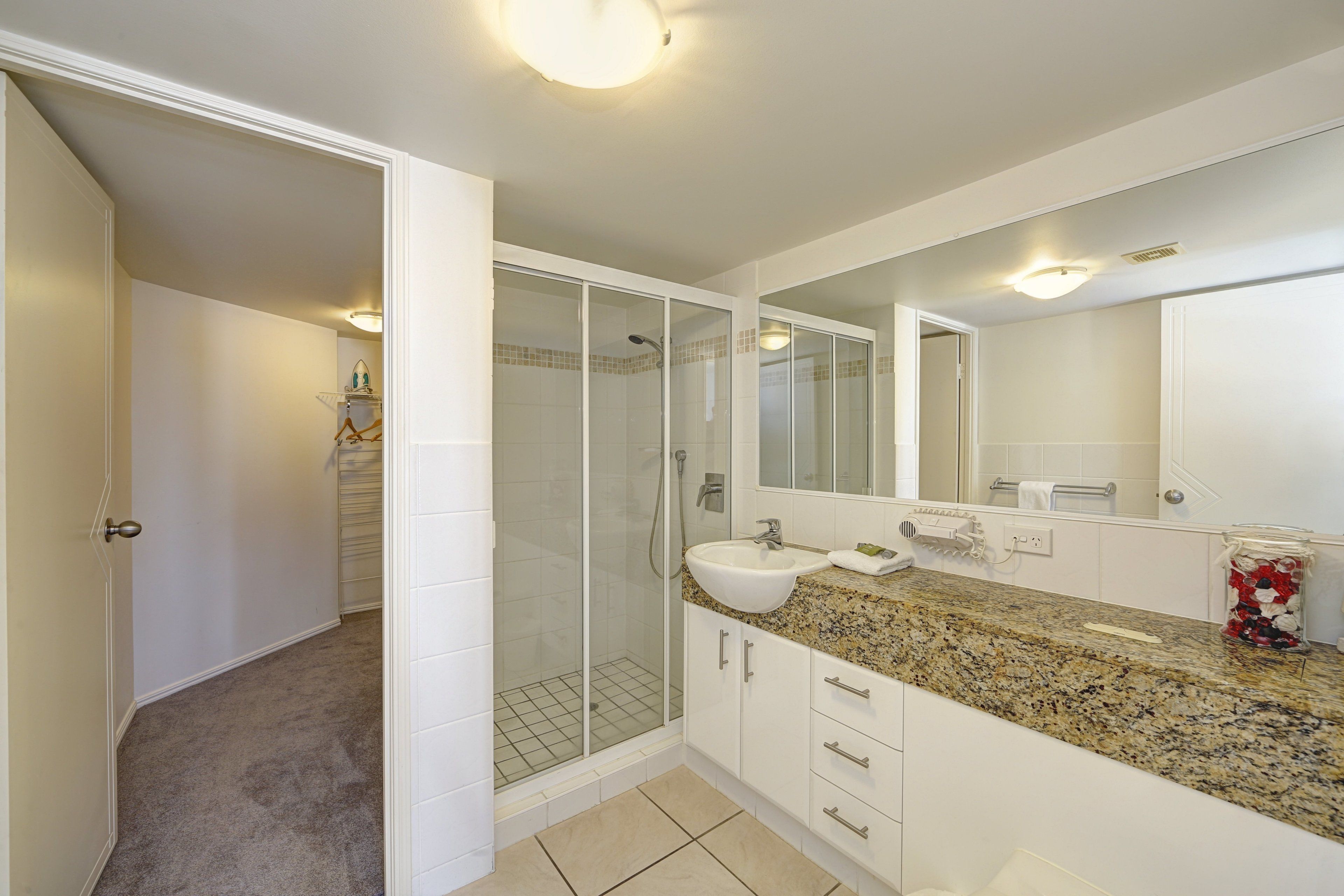 A modern bathroom with a glass-enclosed shower, a granite countertop, and a large mirror.