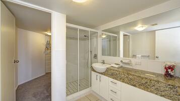 A modern bathroom with a glass-enclosed shower, a granite countertop, and a large mirror.